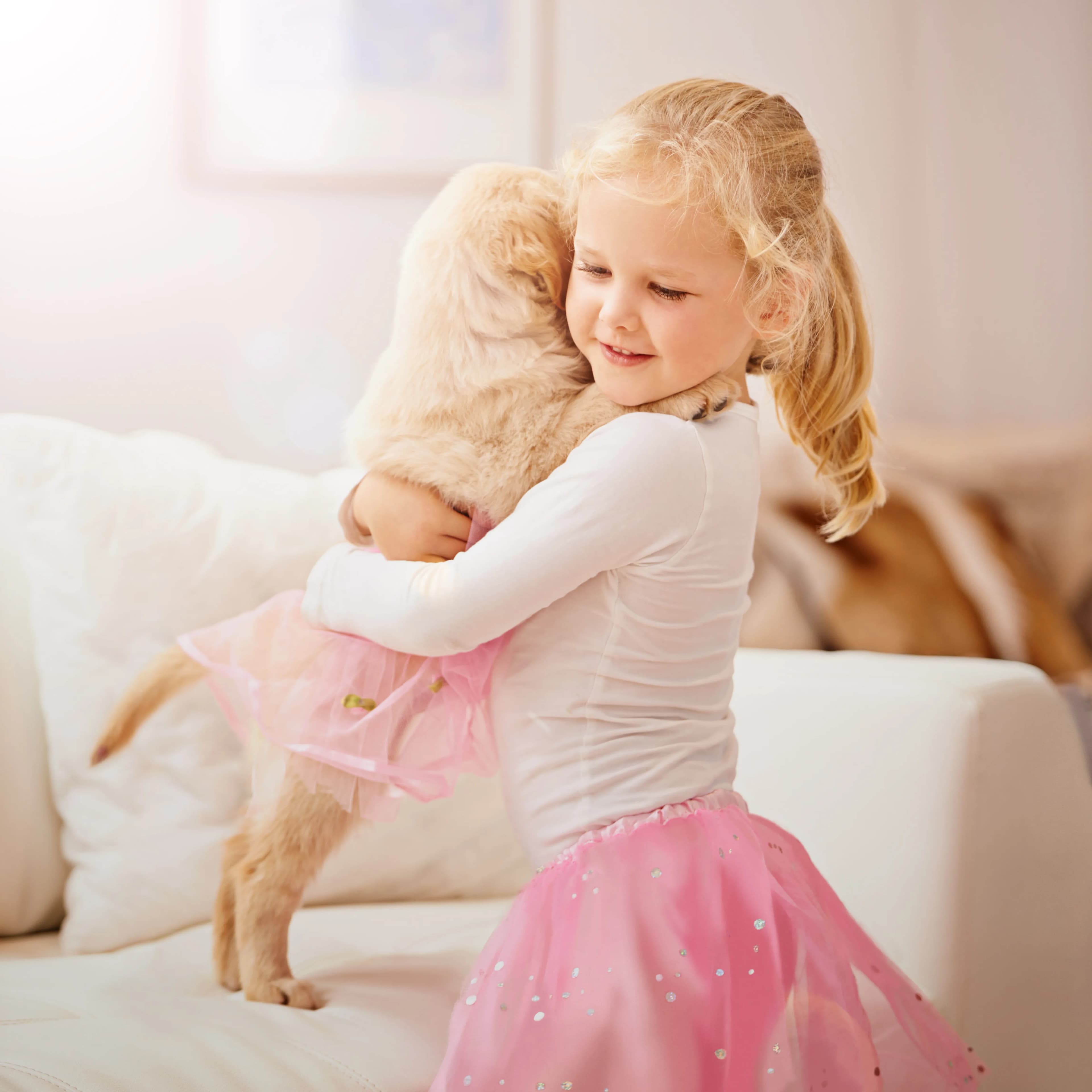 A young girl gently hugging her golden retriever puppy at home